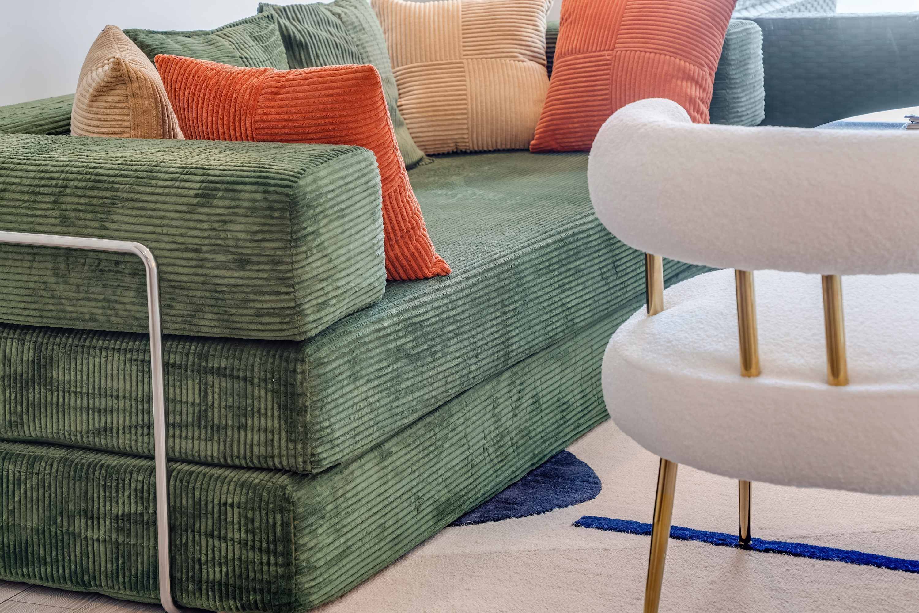 A green sofa with multiple cushions in various colors, a white chair, and a blue rug.