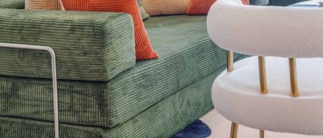 A green sofa with multiple cushions in various colors, a white chair, and a blue rug.