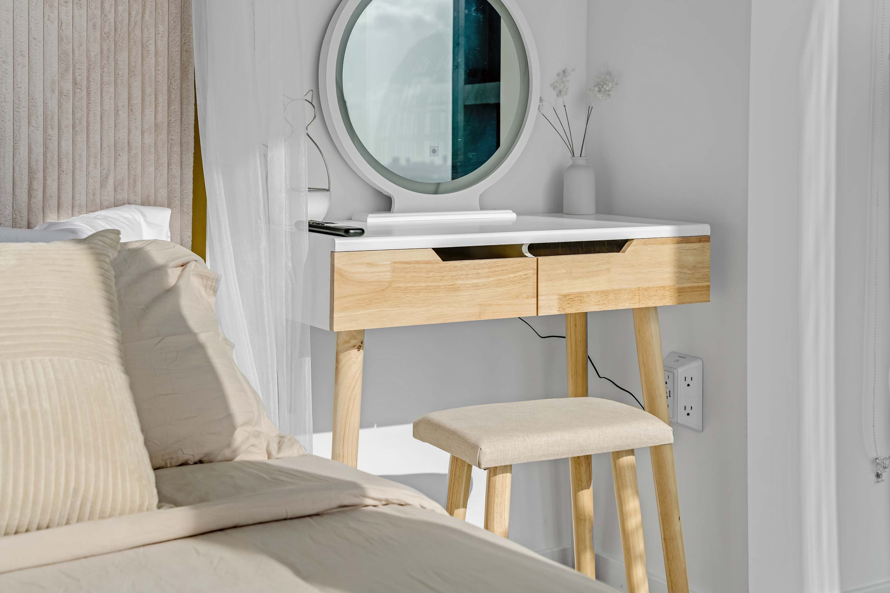 A bedroom with a bed, a bedside table, a mirror, and a small stool.