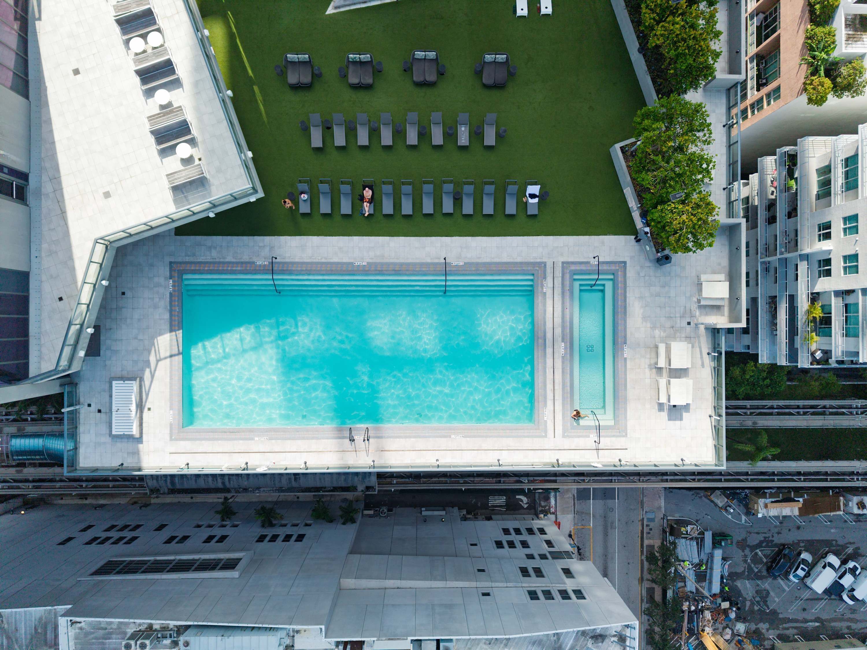 An aerial view of a modern hotel with a large swimming pool, sun loungers, and a rooftop terrace.