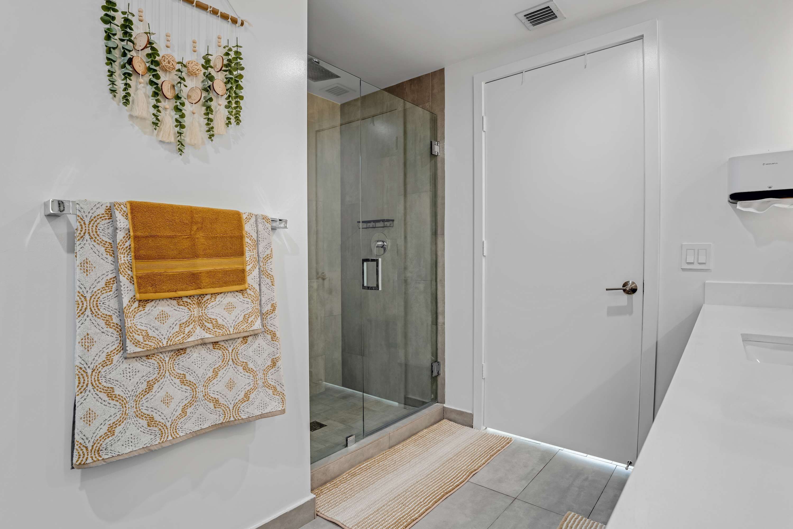 A modern bathroom with a glass shower enclosure, a white sink, and a towel rack with patterned towels.