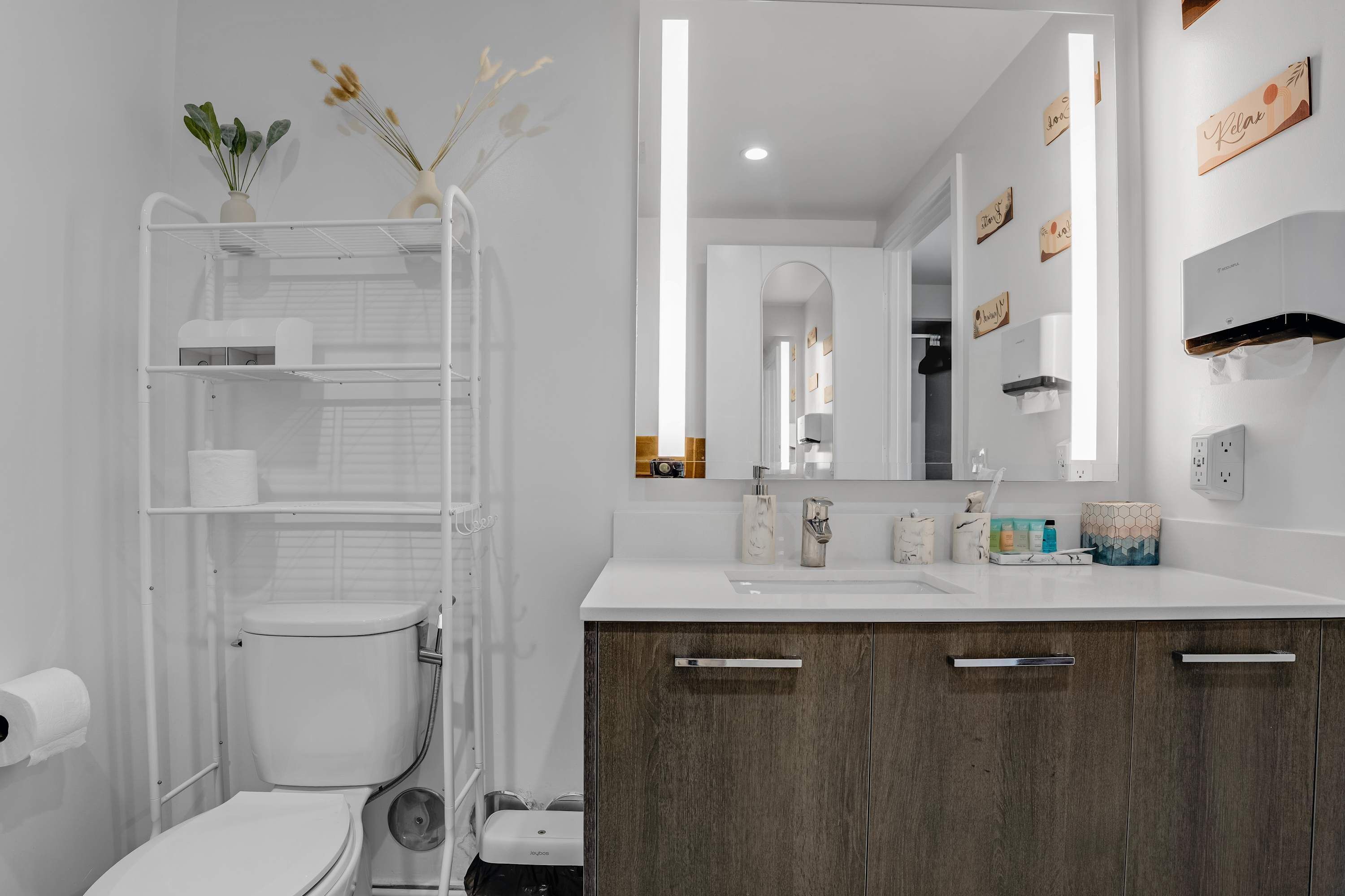 A modern bathroom with a white sink, wooden cabinets, a white toilet, and a towel rack.