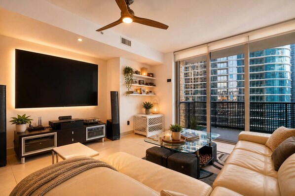 A modern living room with a flat-screen TV, a ceiling fan, a sofa, a coffee table, and a balcony with a city view. - Brickell Skyline Balcony Corner Suite Near City Centre Luxe Pad (Miami)