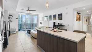 Une cuisine moderne dotée d’un îlot central, d’un coin repas avec un canapé et offrant une vue sur les gratte-ciel grâce à de grandes fenêtres.