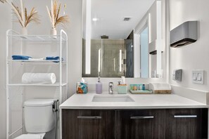 Ein modernes Badezimmer mit einem weißen Waschbecken, dunklen Holzschränken, einer Duschkabine aus Glas und einer weißen Toilette.