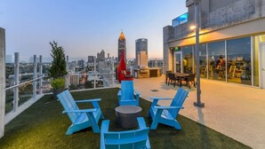 Eine Dachterrasse mit blauen Stühlen, einem roten stuhlförmigen Raketenstuhl und Blick auf die Stadt.