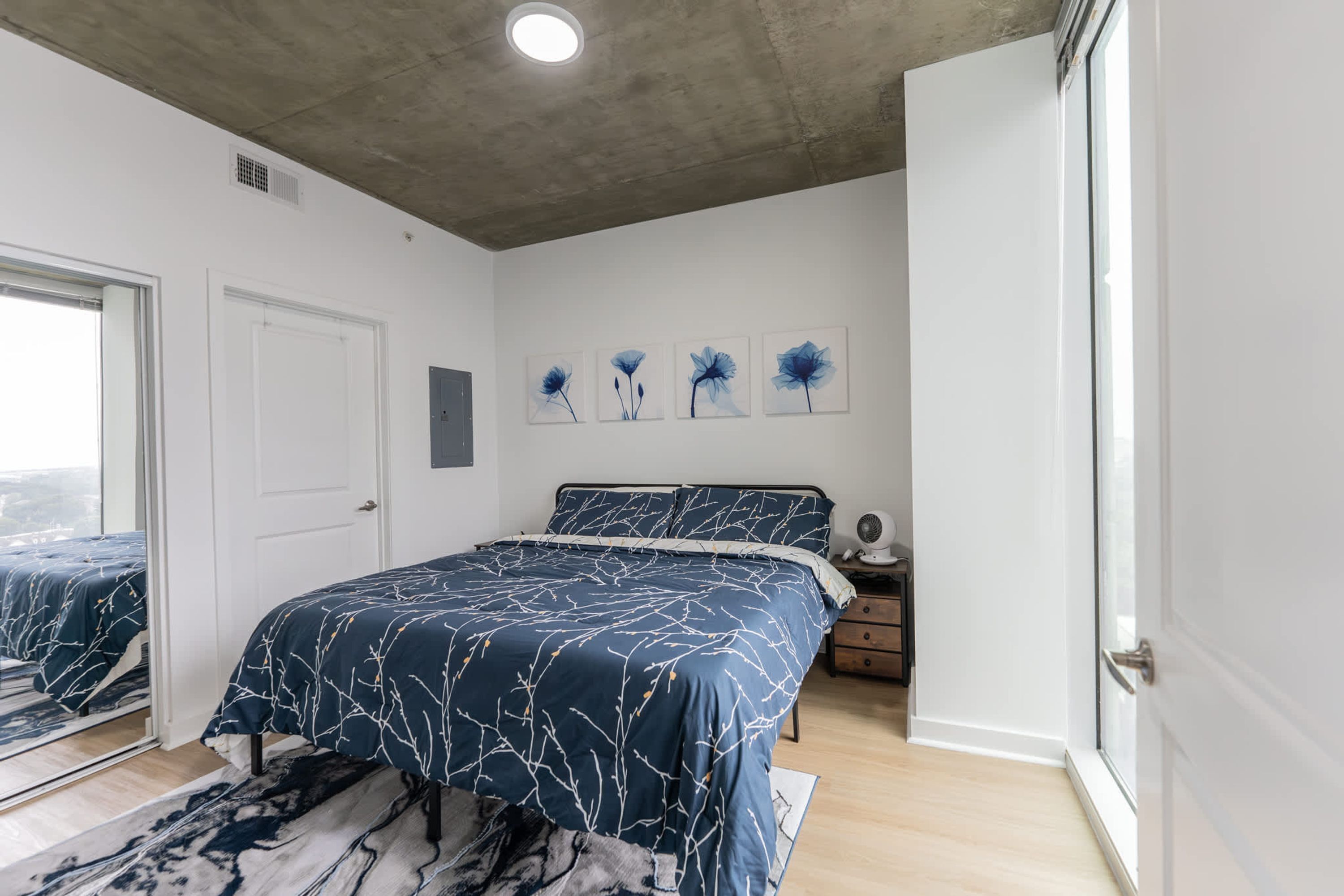 A bedroom with a bed, a nightstand, a window, and a door.