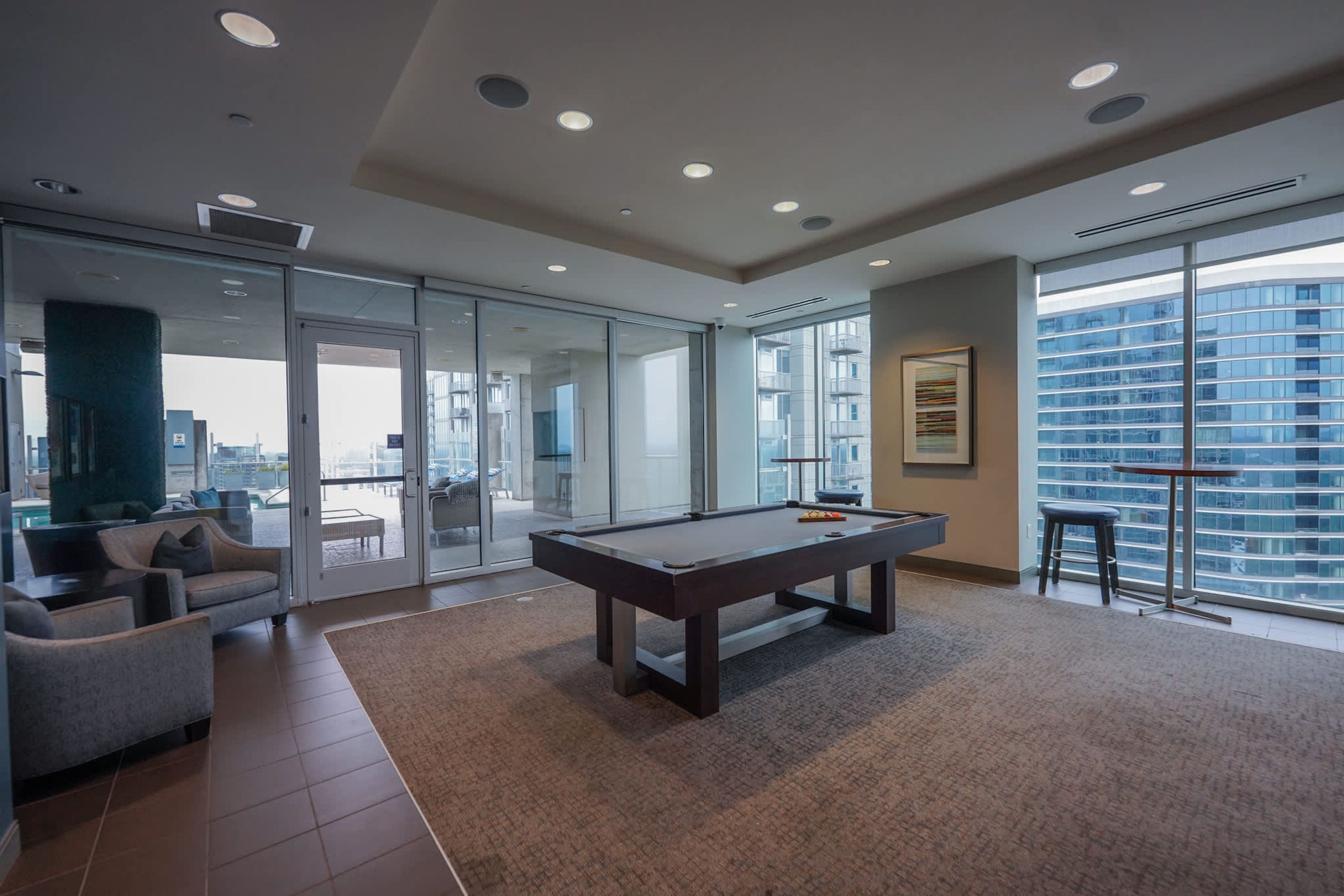 Un salón moderno con mesa de billar, asientos cómodos, amplias ventanas y vistas a la ciudad.