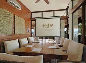 A conference room with a long table, white chairs, and a projection screen displaying a logo. - El Nido Resorts Pangulasian Island (El Nido)