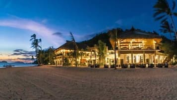 Um hotel à beira-mar com vários andares, área de estar externa e palmeiras.