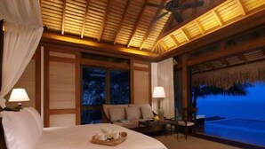 A hotel room with a bed, a nightstand, a table with a tray of items, and a view of the ocean.
