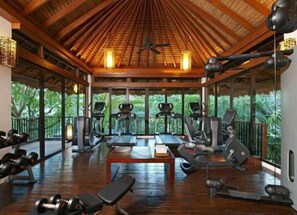 Une salle de sport équipée de tapis de course, de vélos elliptiques et de poids libres, avec de grandes fenêtres et un plafond en bois.