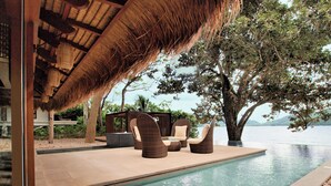 A poolside area with wicker furniture, a thatched roof, and a view of the water.