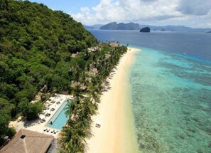 A beach resort with a pool, palm trees, and a clear view of the ocean.