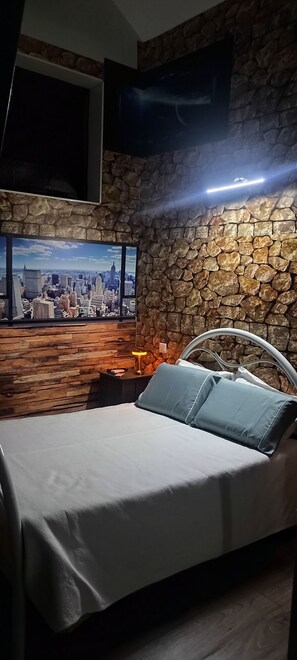 A bedroom with a bed, a TV mounted on a stone wall, and a cityscape view. - Albergue do Visconde (Vila do Conde)