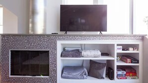 A living room with a fireplace, a TV mounted above it, and shelves with board games. - Bayside Retreat - Bay Views in Walkable Coronado (Coronado)