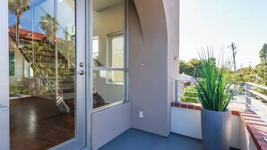 A modern building with a glass door leading to a wooden interior, a potted plant on the balcony, and a clear view of the surrounding area. - Bayside Retreat - Bay Views in Walkable Coronado (Coronado)