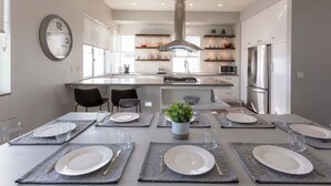 A modern kitchen with a central island, stainless steel appliances, and a dining area set for six. - Bayside Retreat - Bay Views in Walkable Coronado (Coronado)