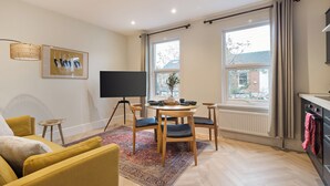 Ein modernes Wohnzimmer mit einer Couch, einem Esstisch mit Stühlen, einem Flachbildfernseher und einem großen Fenster mit Vorhängen.