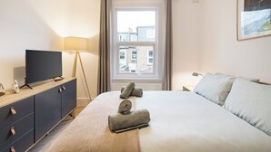 Ein Hotelzimmer mit einem Bett, einem Fernseher auf einer Kommode, einer Lampe und einem Fenster mit Vorhängen.