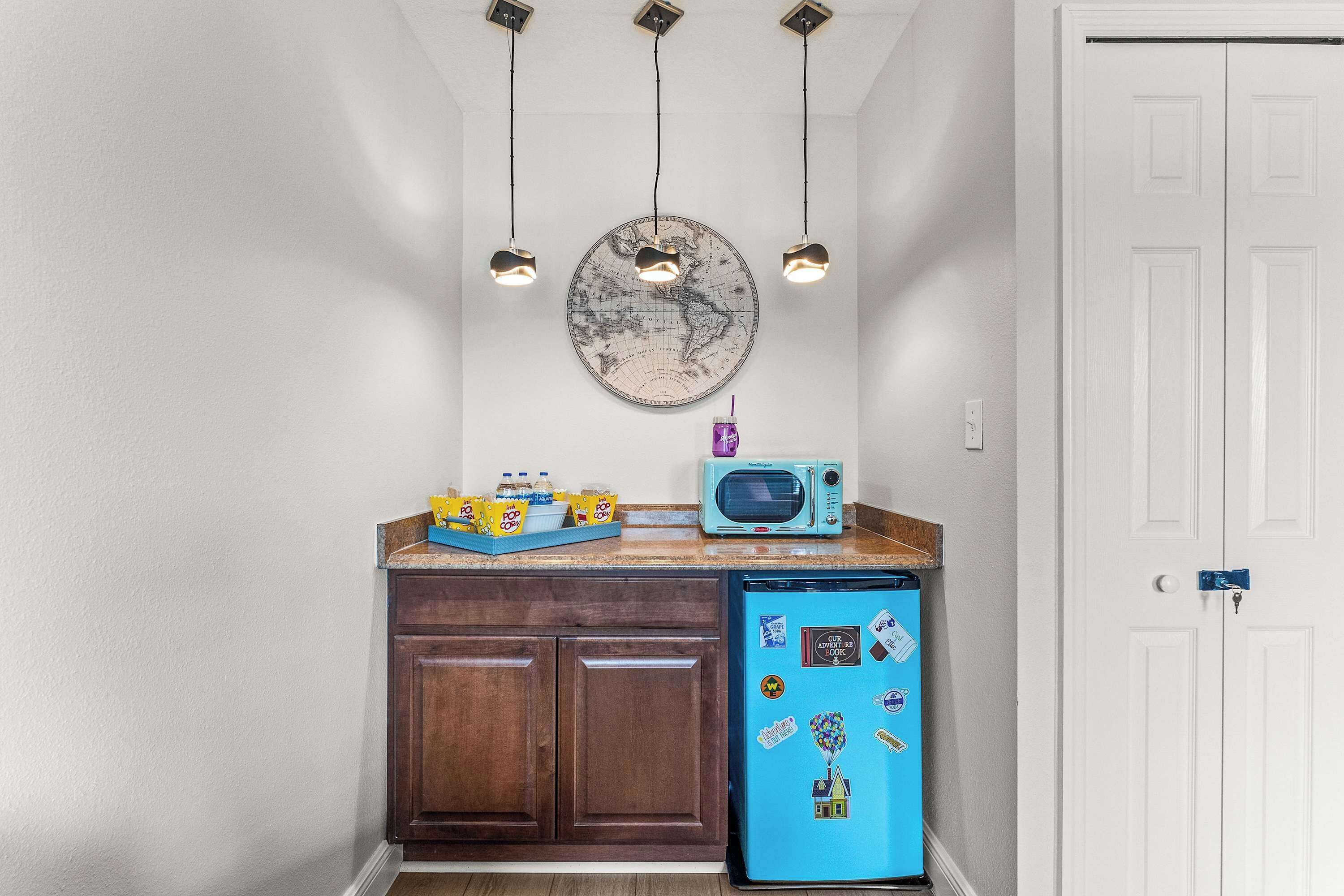 Une cuisine avec un réfrigérateur bleu, des armoires en bois, un four à micro-ondes et des luminaires suspendus.