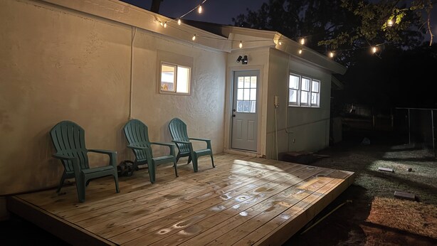 Un pontile in legno con tre sedie e un piccolo edificio con una porta e finestre, illuminato da luci a stringa.