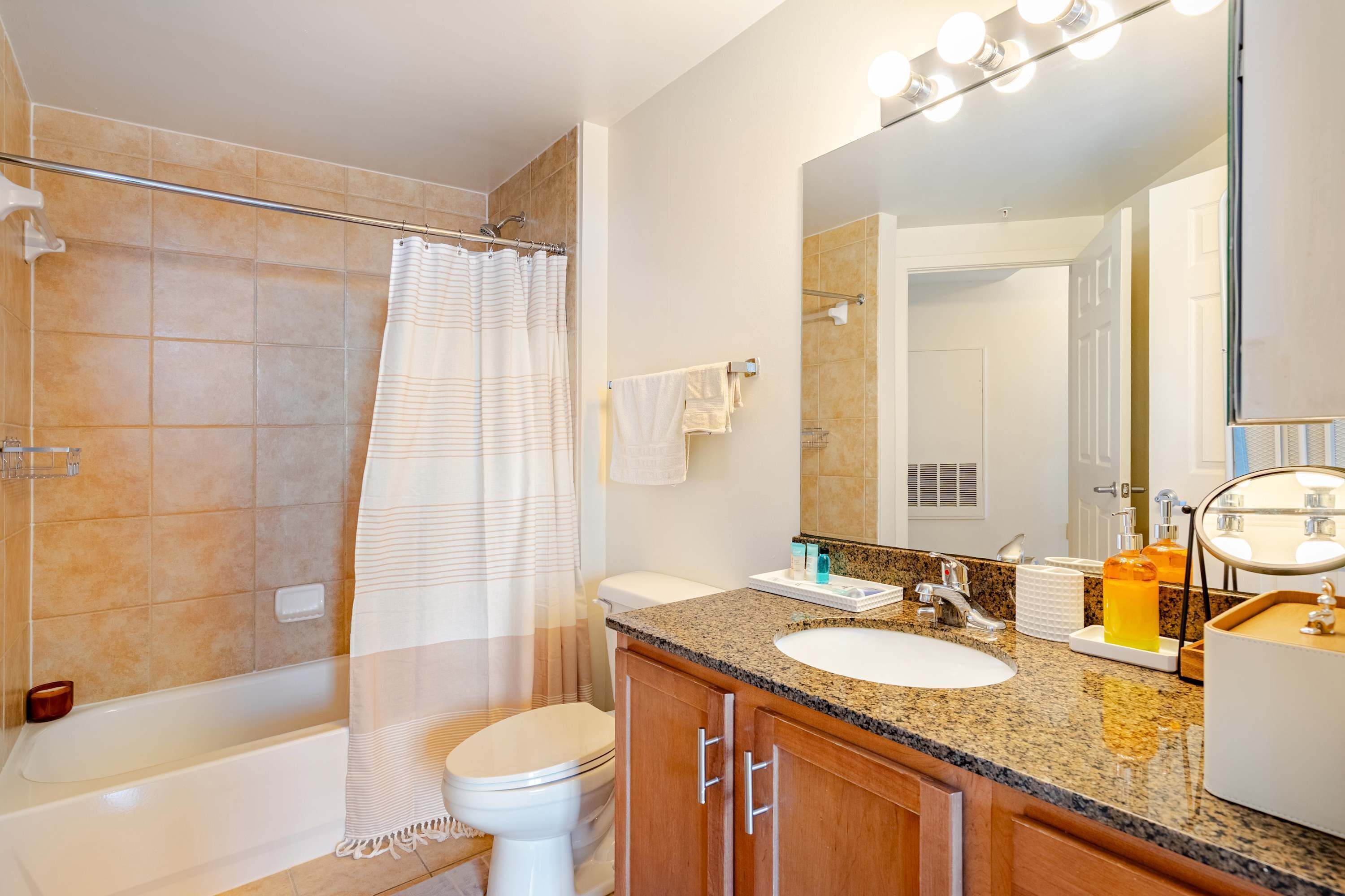 A bathroom with a shower, toilet, vanity, and a large mirror.