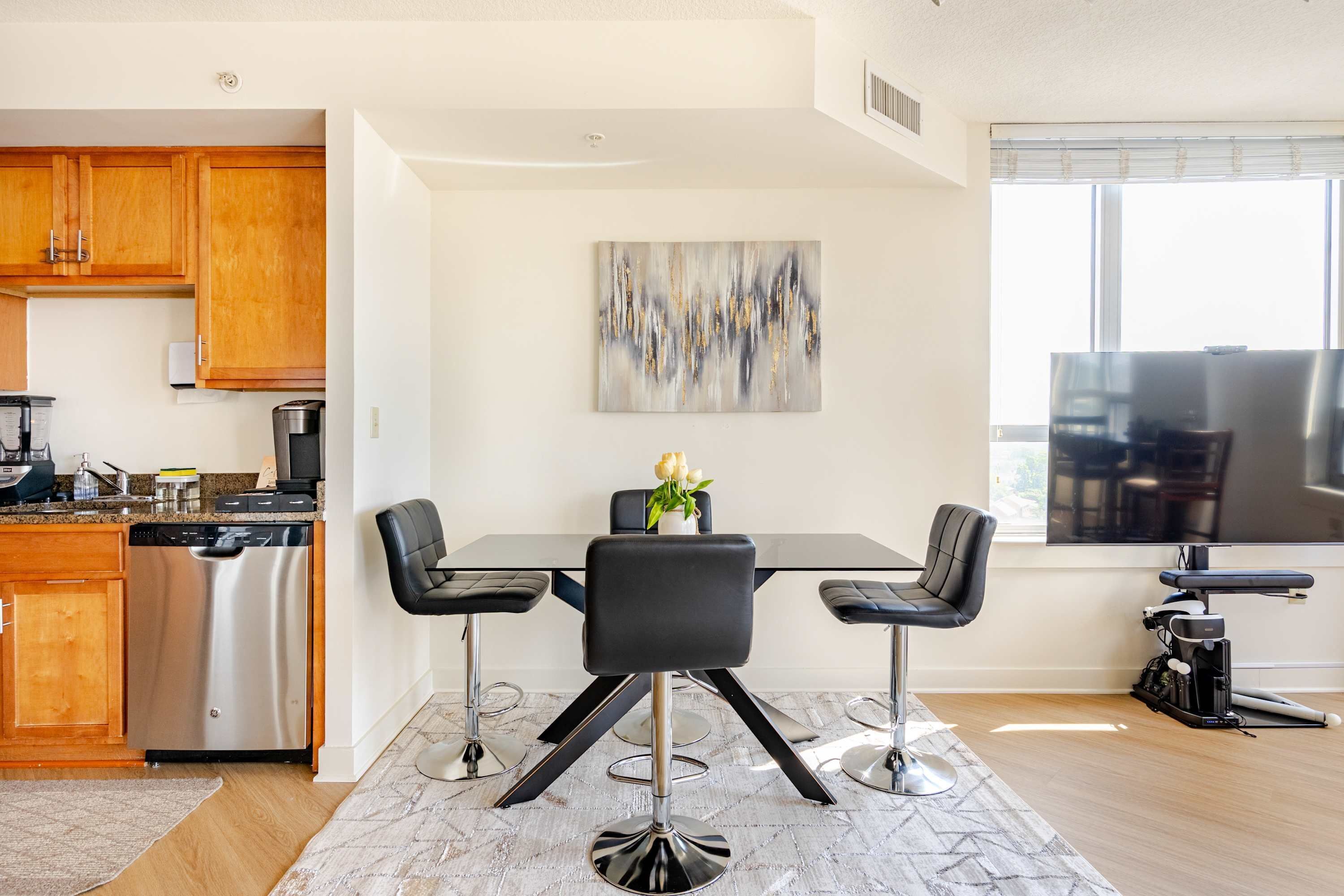 A modern kitchen with wooden cabinets, a stainless steel dishwasher, and a dining area with a black table and chairs.