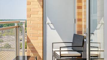 Un balcón con puerta de cristal, dos sillas y una mesa de metal.