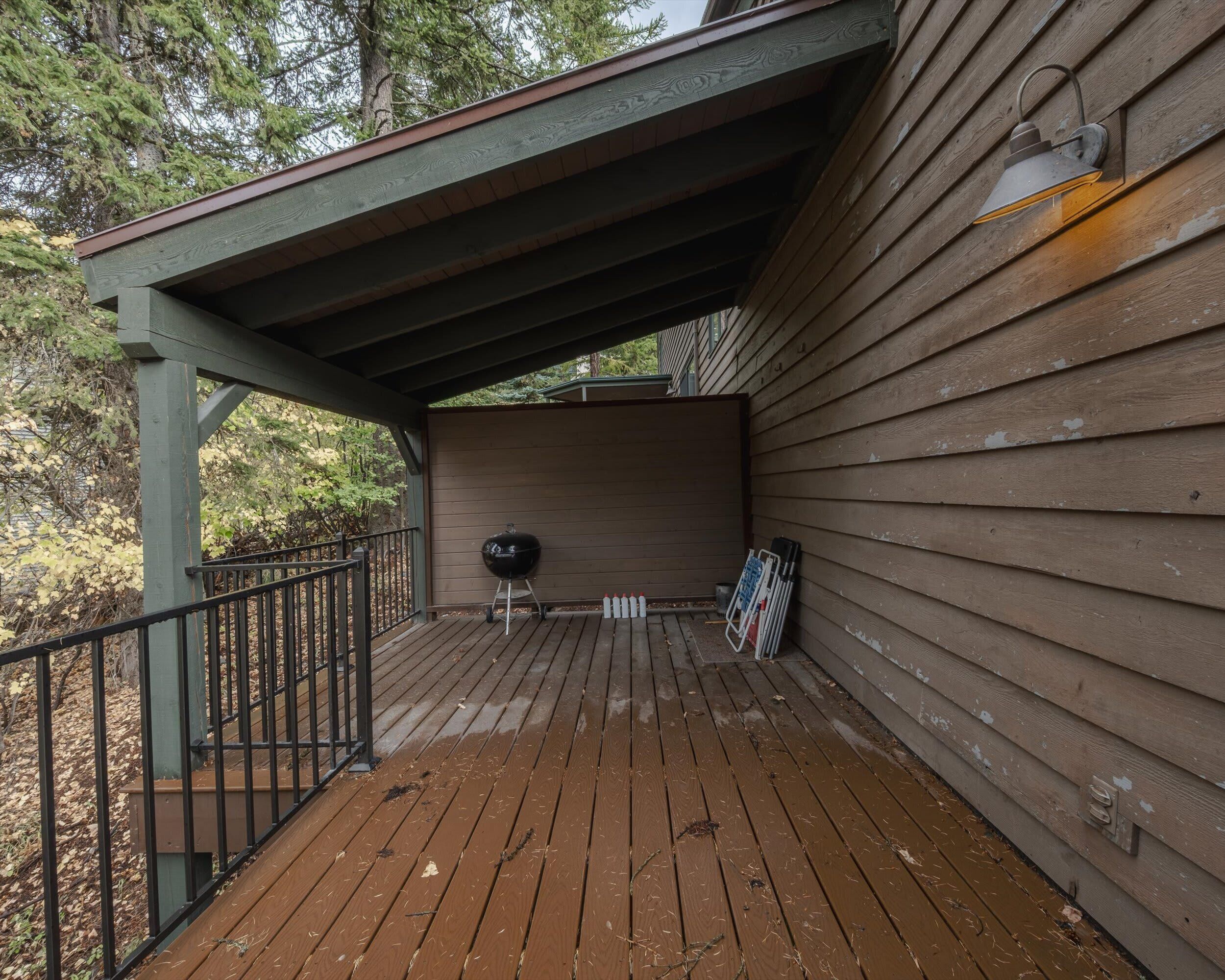 Une terrasse en bois avec un barbecue, une rambarde en métal et un luminaire fixé au mur.