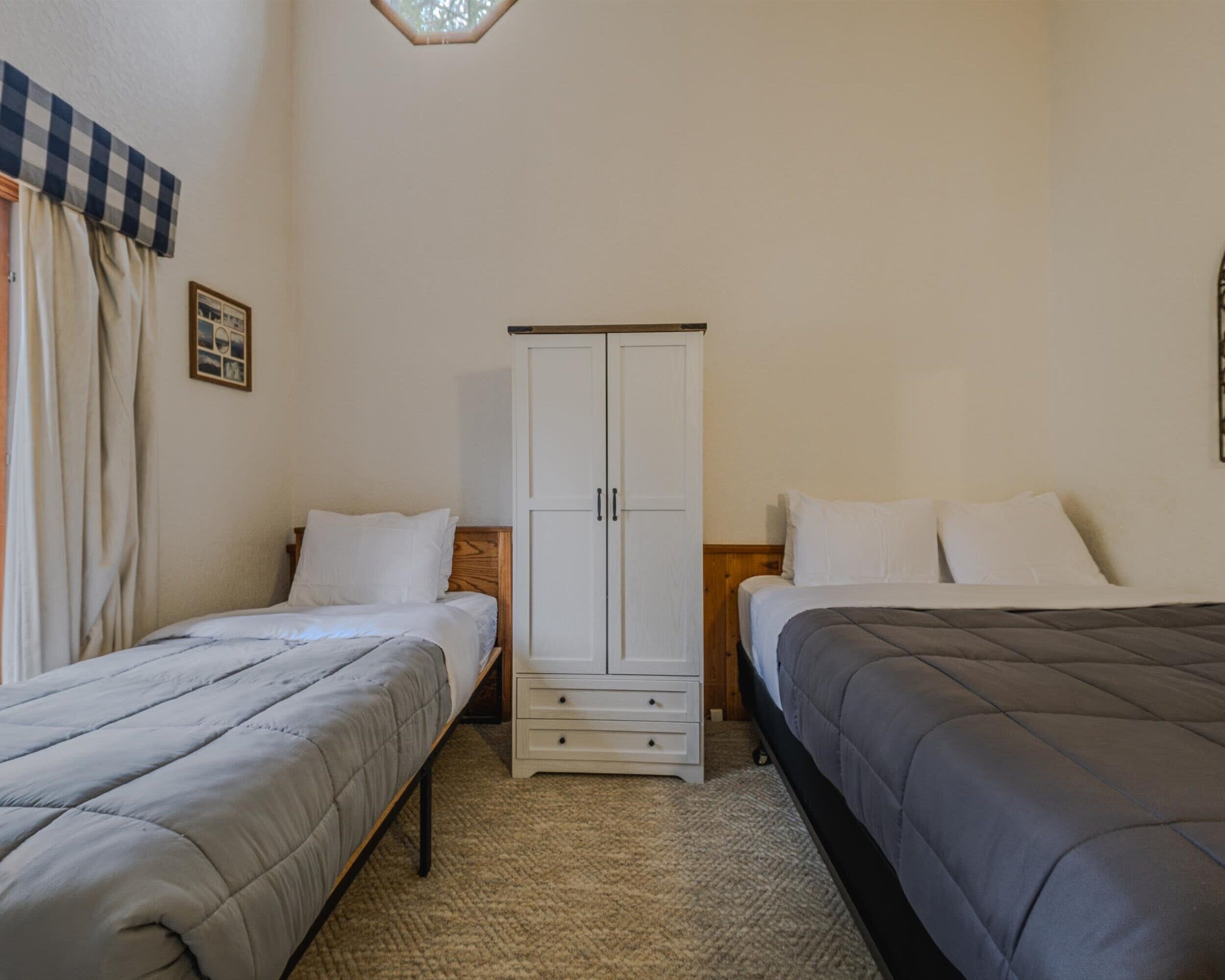 Una habitación con dos camas individuales, un armario y un pequeño cuadro en la pared.