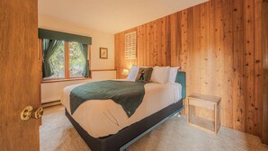 A bedroom with a bed, a nightstand, a window with curtains, and wooden paneling on the walls. - Sans Souci 1 3 Bedroom Ski In, Ski Out Retreat (Whitefish)