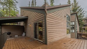 A wooden deck with a covered area and a sliding glass door leading to an interior space. - Sans Souci 1 3 Bedroom Ski In, Ski Out Retreat (Whitefish)