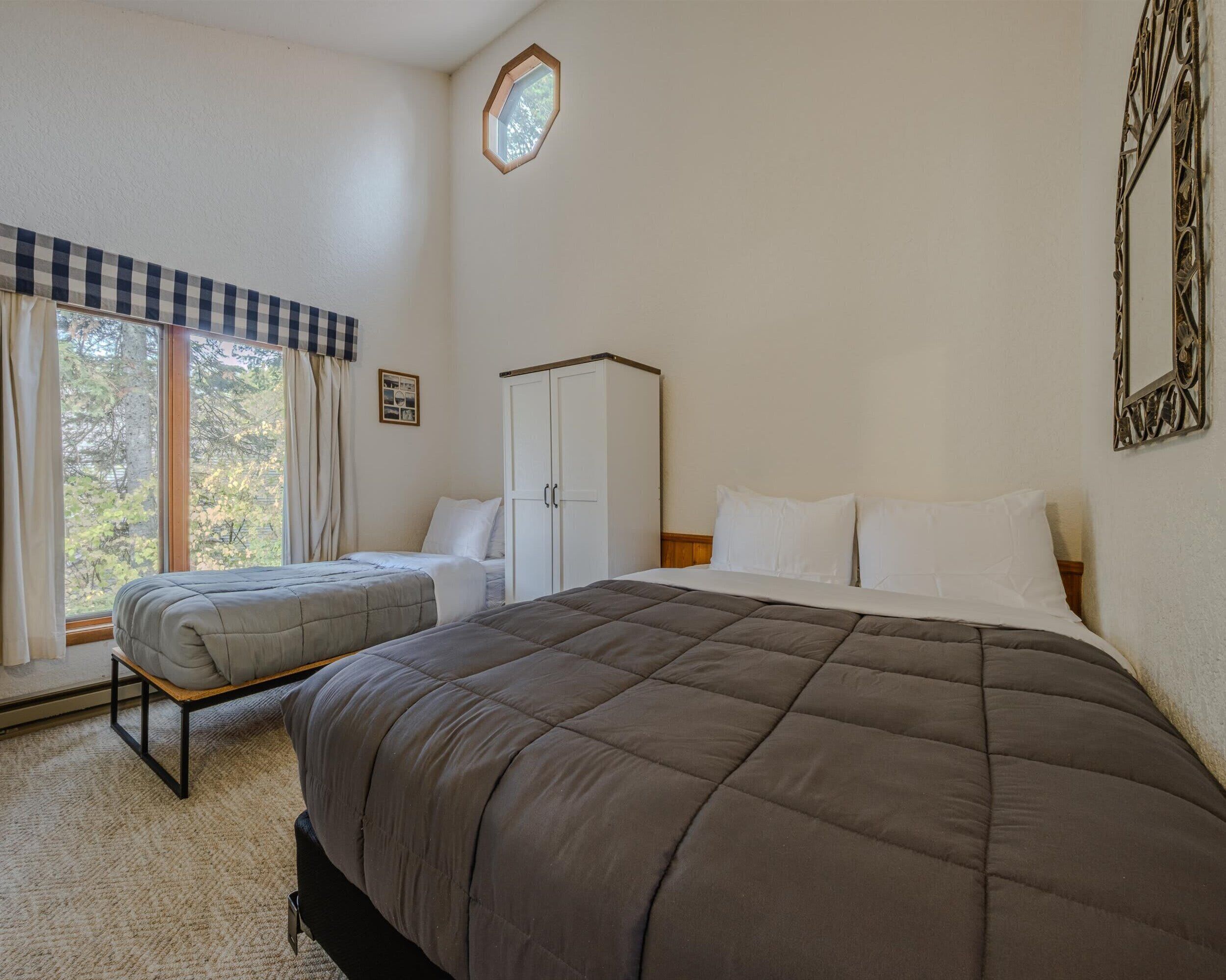 Een slaapkamer met een groot bed, een kleiner bed, een kledingkast en een raam met gordijnen.