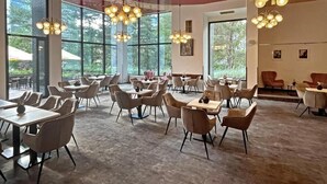 A spacious indoor area with multiple tables and chairs, large windows, and hanging light fixtures. - Hotel ILF (Prague)