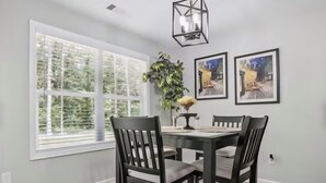 Un coin repas avec une table et des chaises, une plante en pot et des œuvres d’art encadrées accrochées au mur.