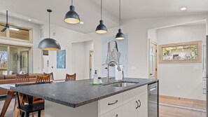 Una cucina moderna con isola centrale, illuminazione a sospensione e vista sull'area pranzo.