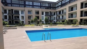 Un bâtiment moderne doté d’une piscine, de nombreux balcons et d’une cour intérieure agrémentée de plantes.