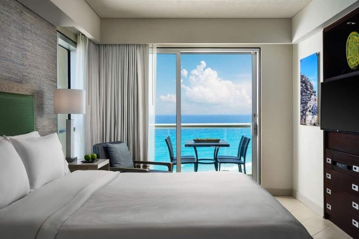 A hotel room with a large bed, a balcony with a table and chairs, and a TV on the wall.