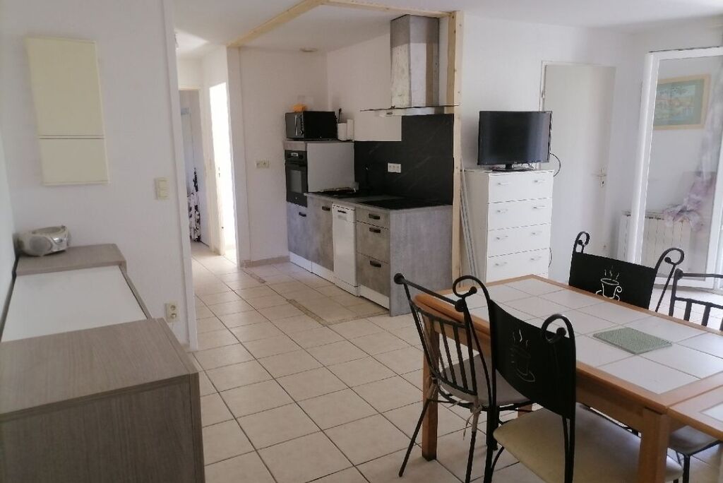A compact kitchen with a dining area, including a table and chairs, and a television on a cabinet.