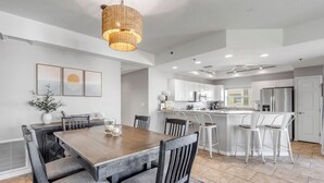 Une cuisine moderne avec des meubles blancs, un îlot central doté de tabourets de bar et un coin repas avec une table et des chaises en bois.