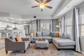 A modern living room with a ceiling fan, a gray sofa, a gray armchair, and a patterned rug. - Spacious 3BR Ocean Walk Condo • Multiple Decks (New Smyrna Beach)