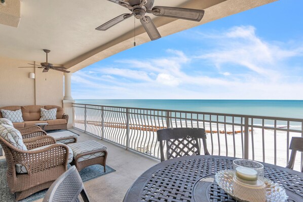 A balcony with wicker furniture, a table with a glass container, and a view of the beach.