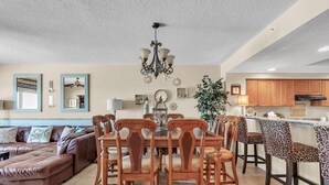 Un salón amplio con un sofá seccional de cuero marrón, una mesa de comedor de madera con sillas y una zona de cocina con armarios de madera y encimera.