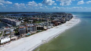 Vista aérea de una ciudad costera con una extensa playa de arena, un puerto deportivo y un denso conjunto de hoteles y edificios a lo largo de la costa.
