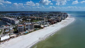 Vista aérea de una ciudad costera con una extensa playa de arena, un puerto deportivo y un denso conjunto de hoteles y edificios a lo largo de la costa.