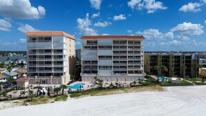 Un hotel frente a la playa con varios pisos, balcones y una zona de piscina.