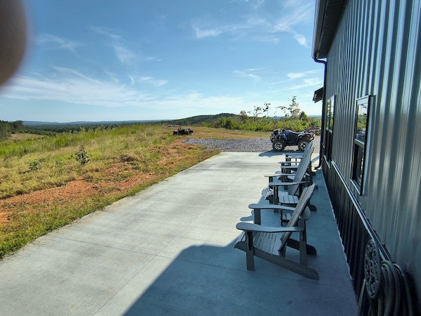 Une terrasse en béton avec des sièges extérieurs et une vue sur un chemin de gravier menant à un véhicule.