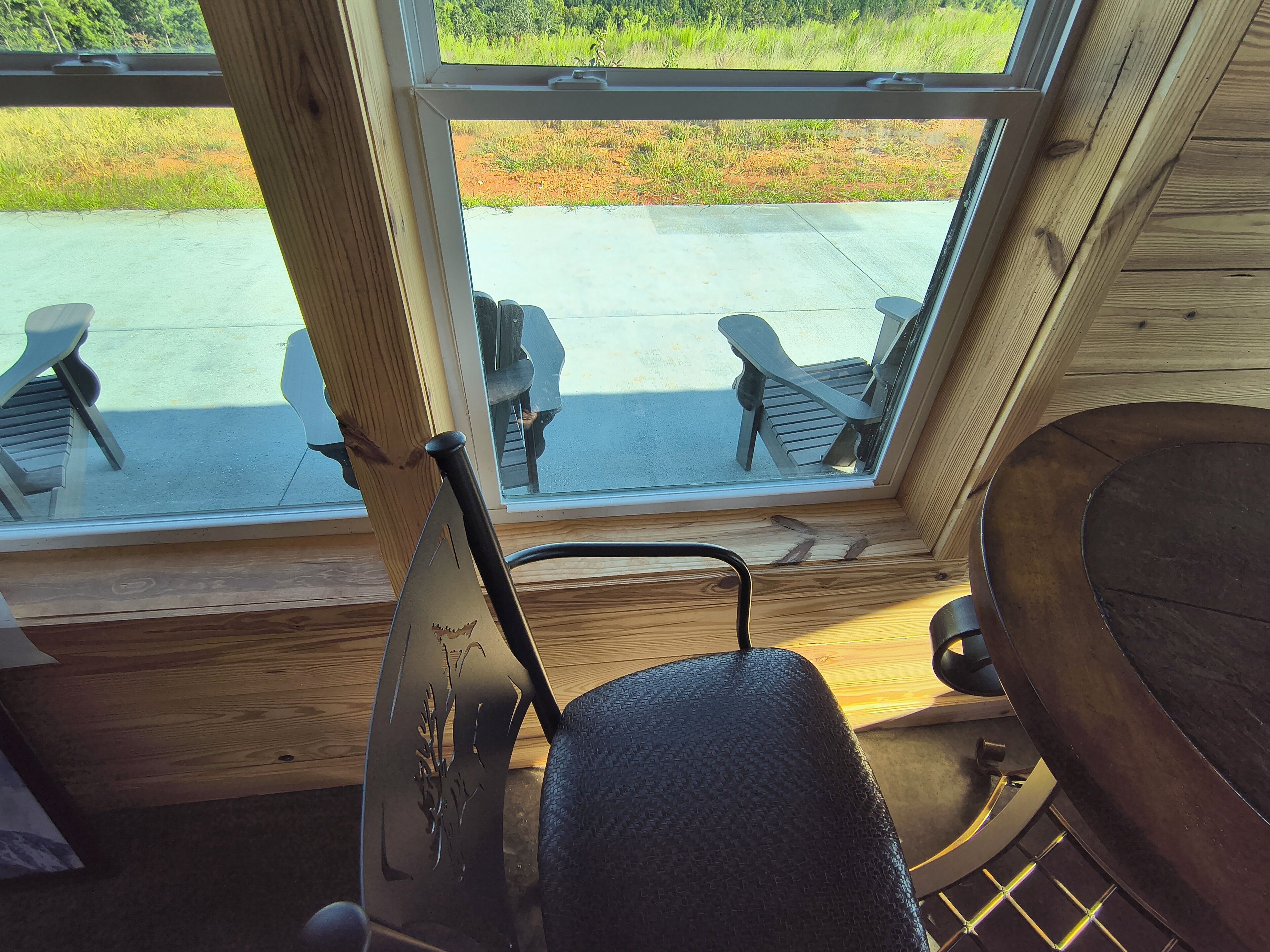 Ein Fenster mit Holzrahmen und Blick auf eine Beton-Terrasse sowie Gartenmöbel.
