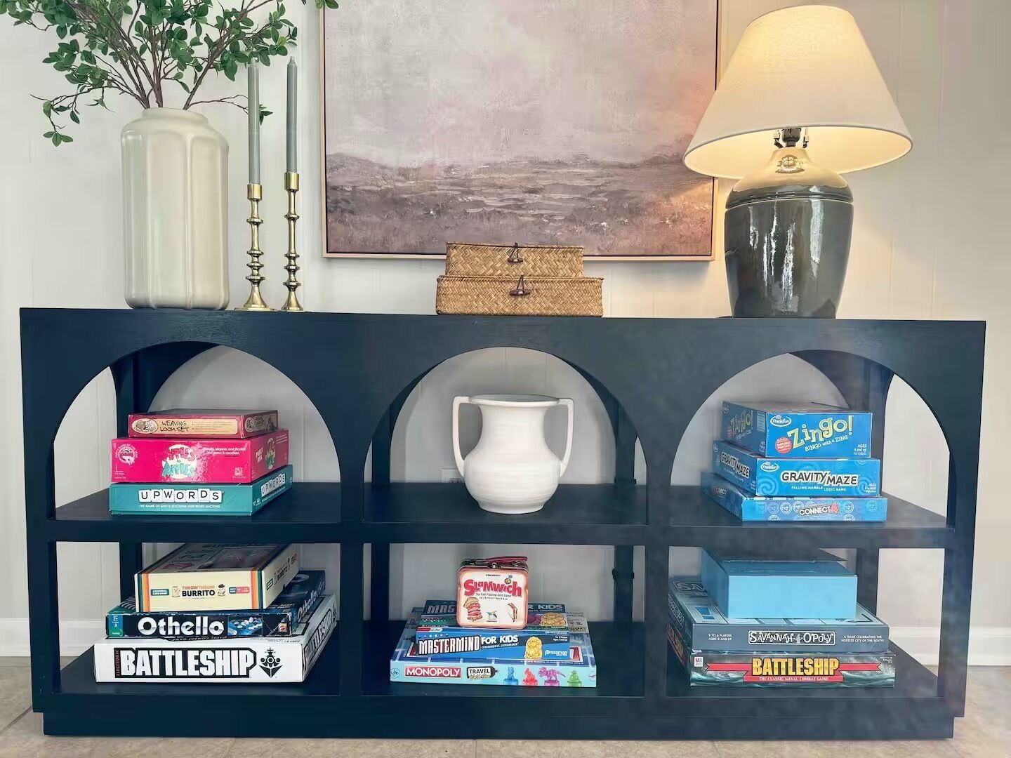 Una estantería con juegos de mesa y una jarra blanca.